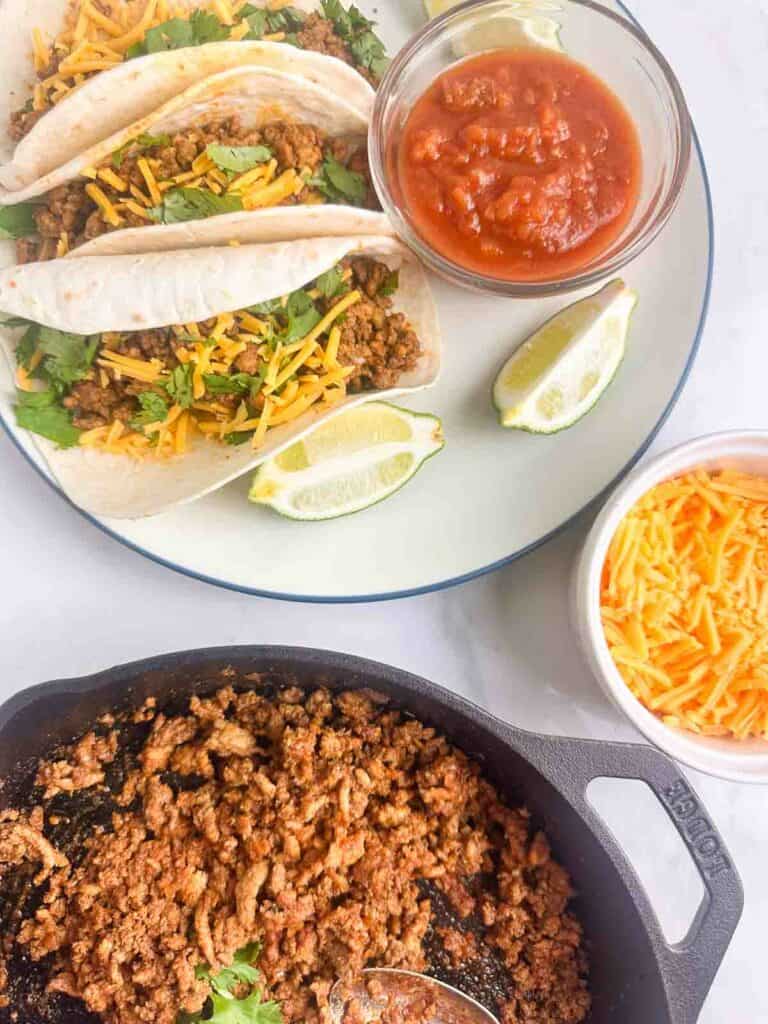 Ground chicken tacos with salsa, cheese, lime, and a cast iron skillet with more.