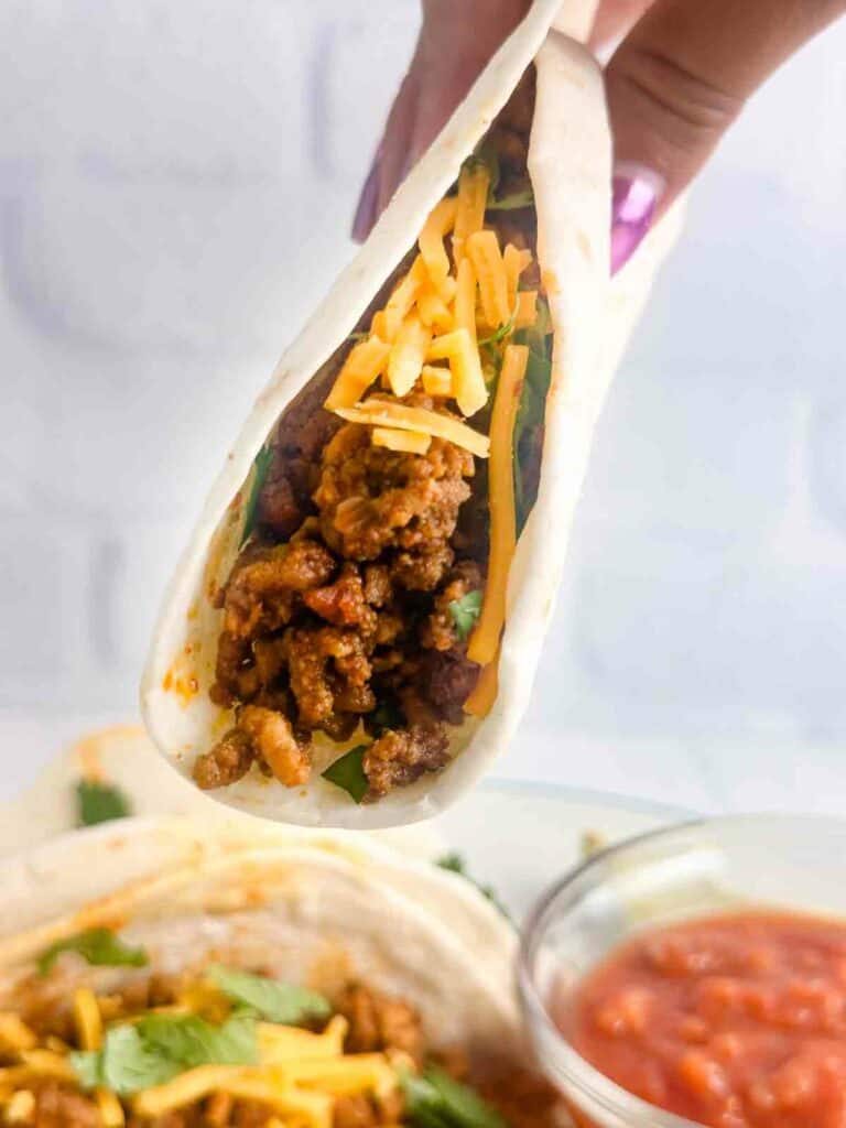 Picking up a ground chicken taco with salsa and more tacos in background.