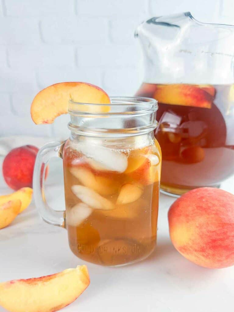 Mason jar of peach tea with ice and peach slices.