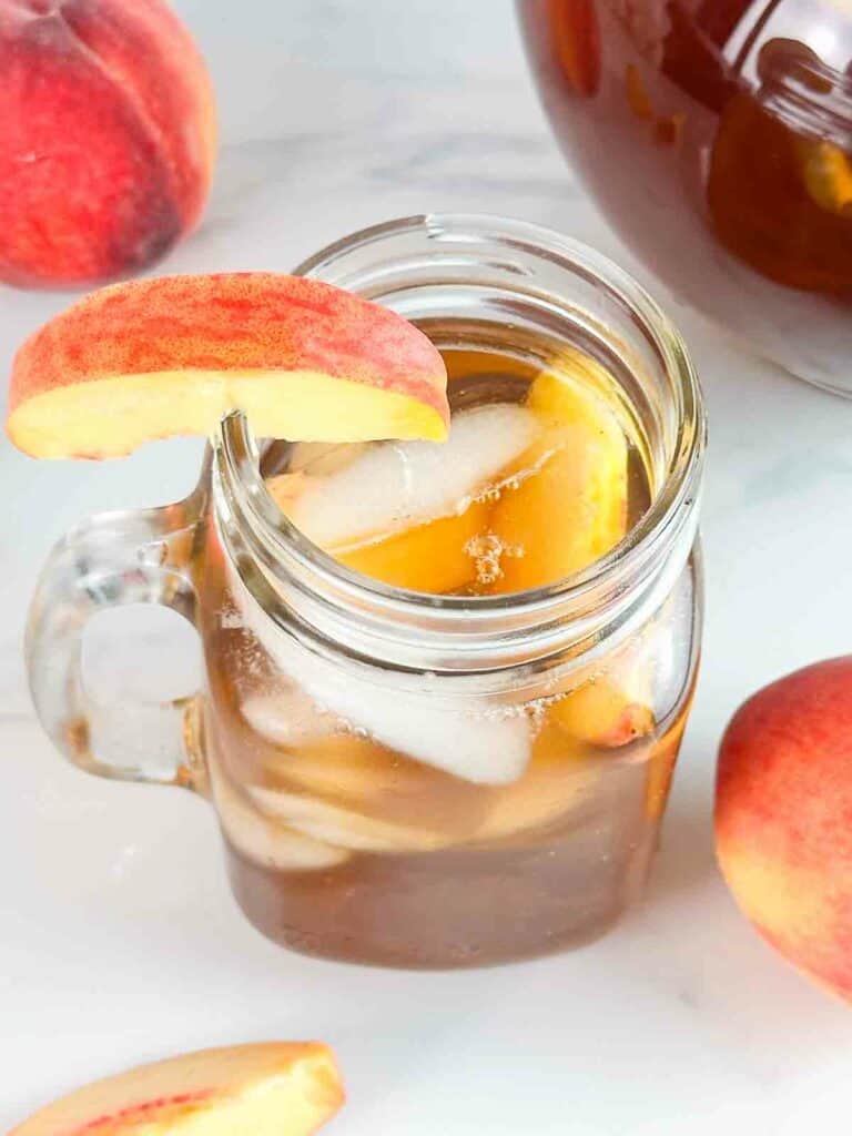 Mason jar of peach tea with ice and peach slices.