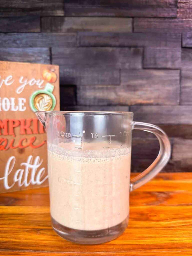 Measuring cup of homemade pumpkin spice coffee creamer recipe in front of a dark background.