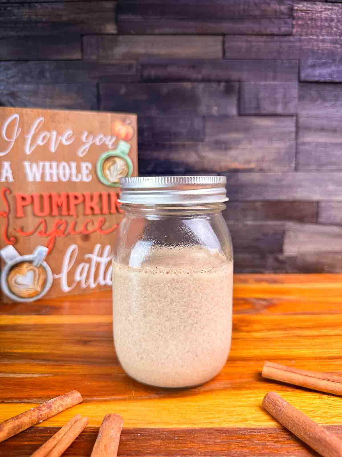 Mason jar of pumpkin spice coffee creamer in front of a dark background.