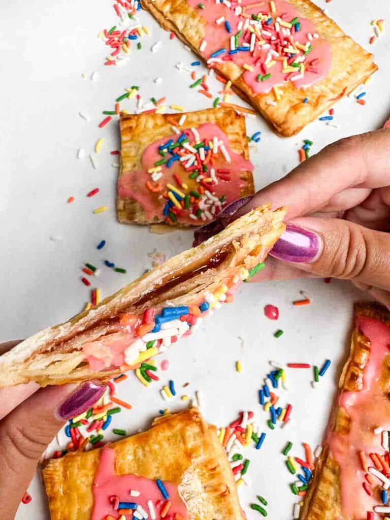 A homemade strawberry pop tart cut in half and being held so the filling shows