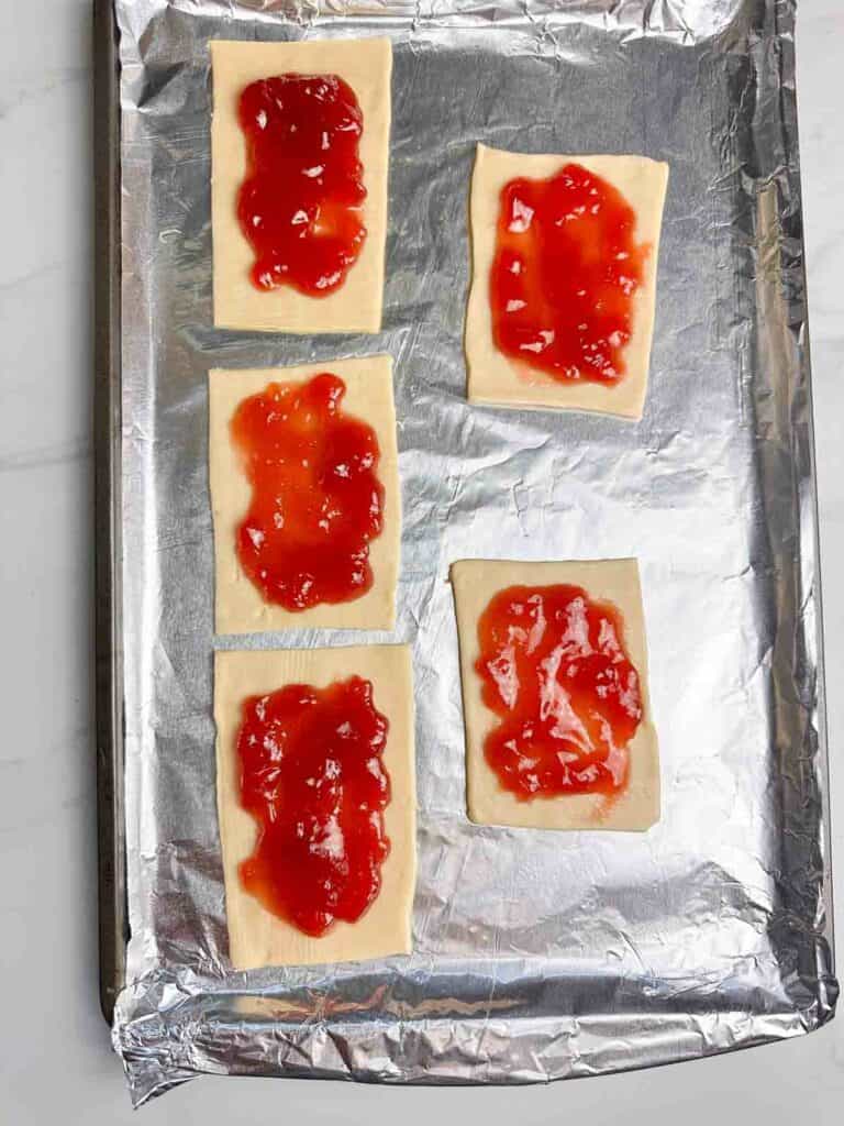 Spread jam on the pie crust rectangles, leaving a border around the edges.