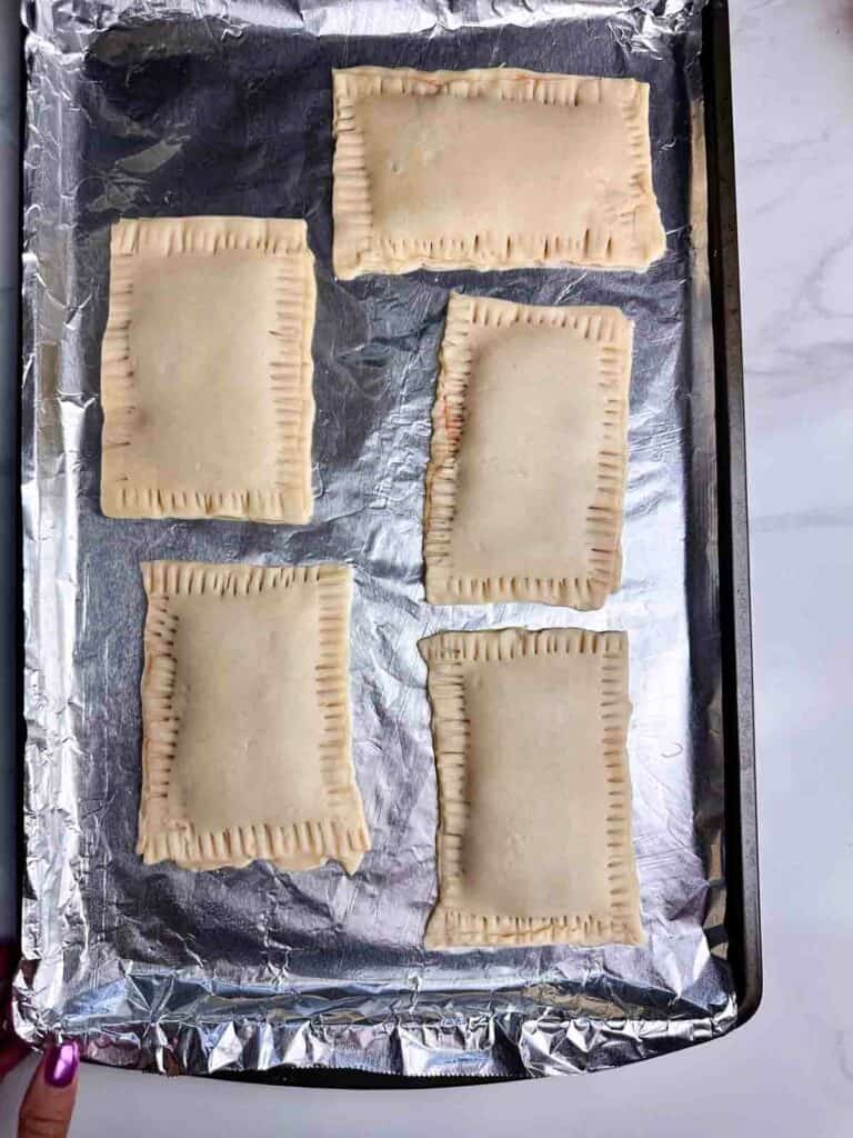 5 unbaked homemade strawberry pop tarts with crimped edges on a baking tray