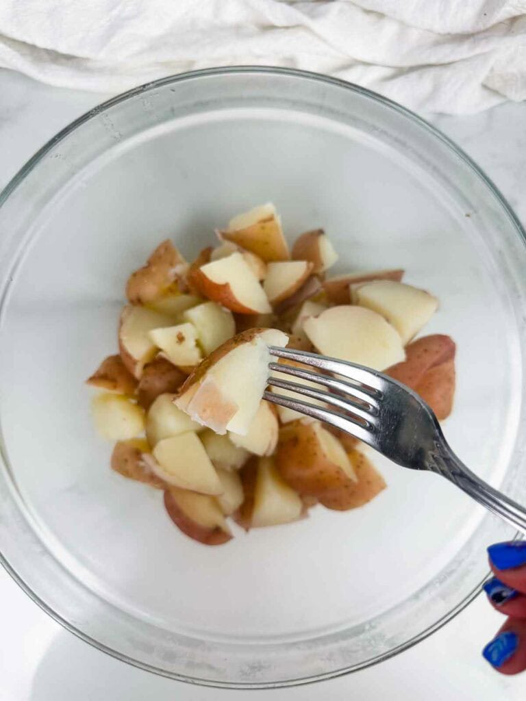 Fork tender red skinned potatoes being held up with a fork over a bowl.