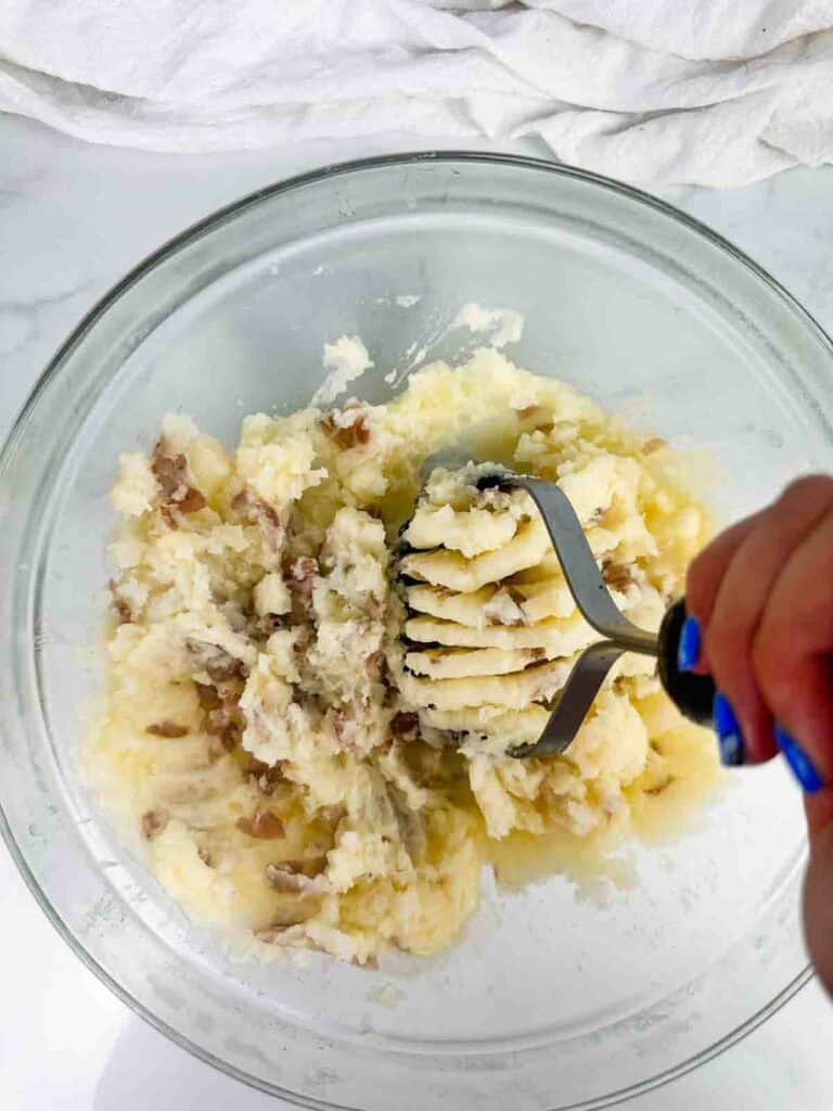 Mashing potatoes with red skins in a clear a bowl.