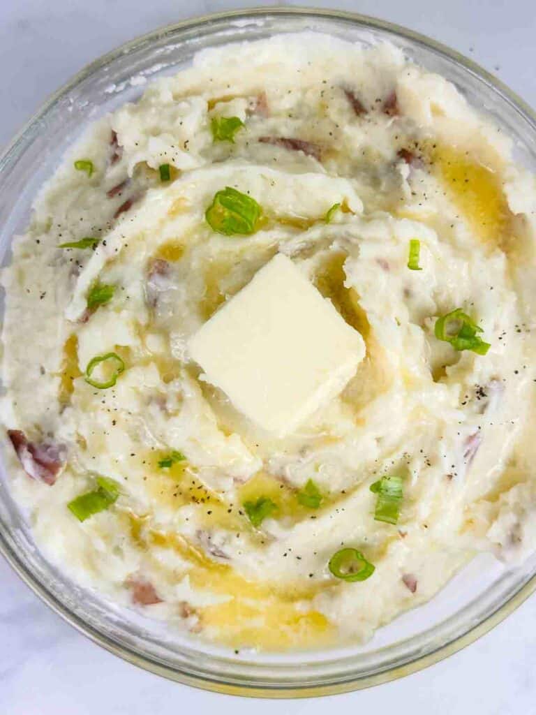 Mashed potatoes with red skinned with green onions and pad of butter on top.