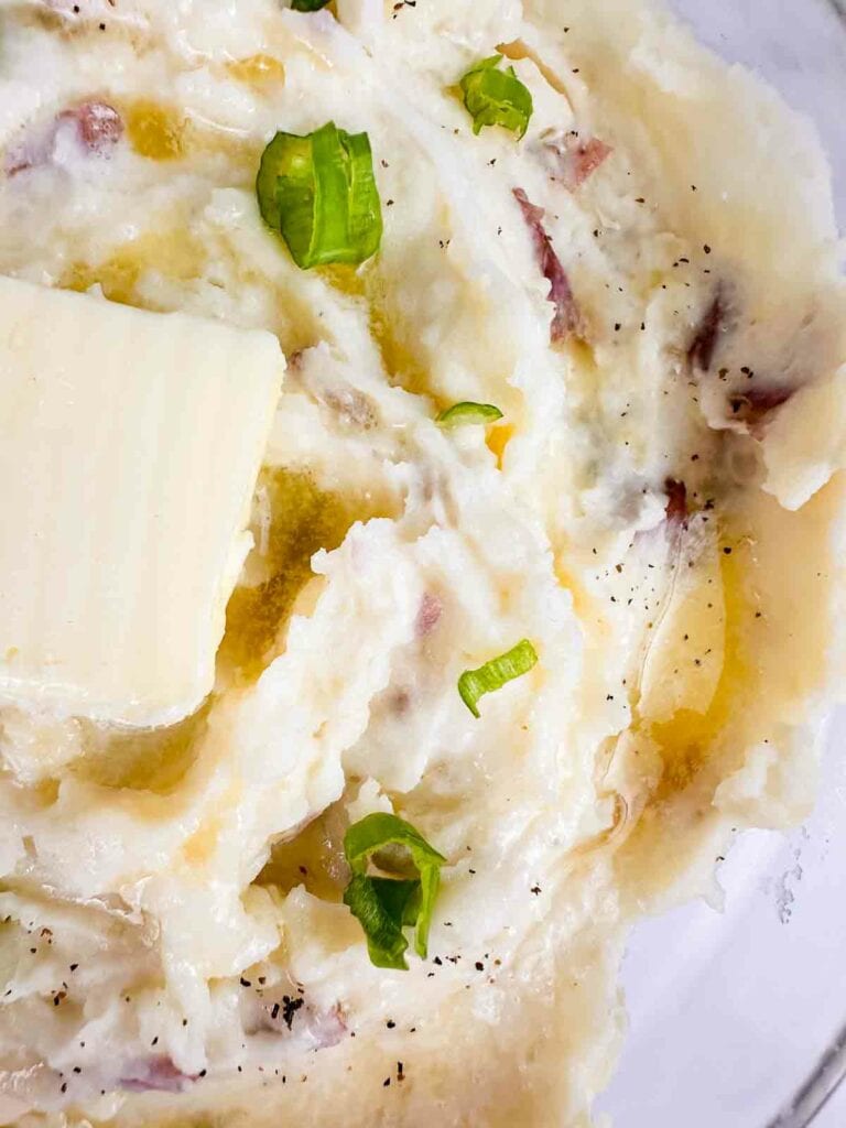 Mashed potatoes with red skinned with green onions and pad of butter on top.