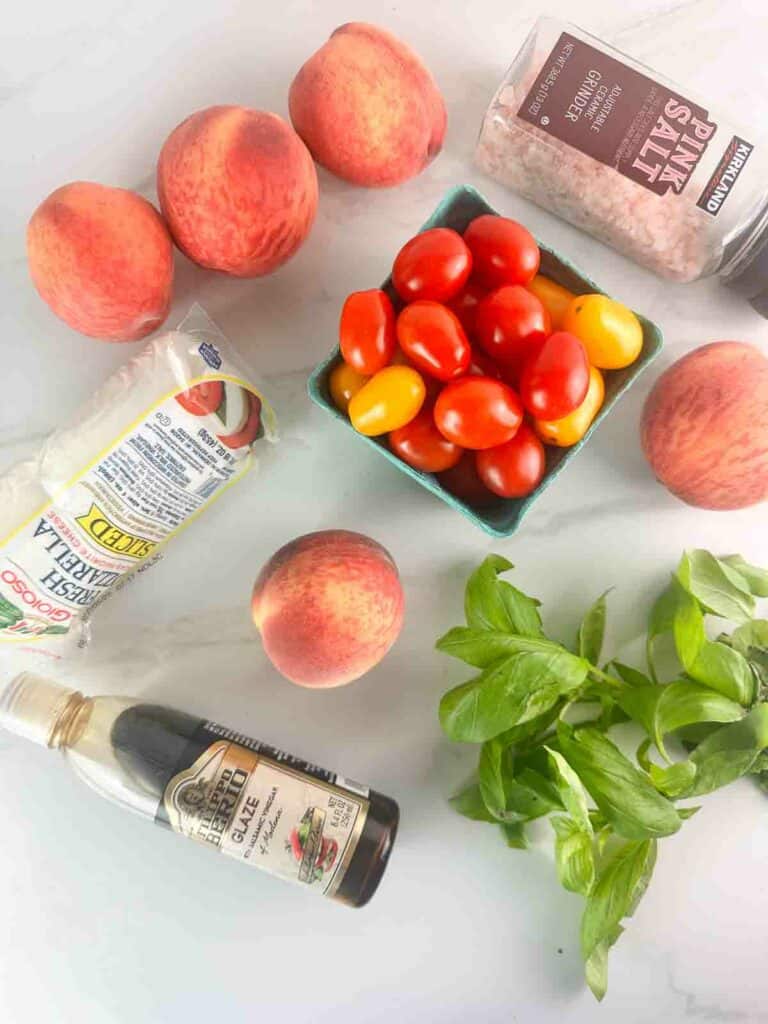 Ingredients for peach caprese salad: peaches, fresh mozzarella, cherry tomatoes, salt, balsamic glaze, and basil.