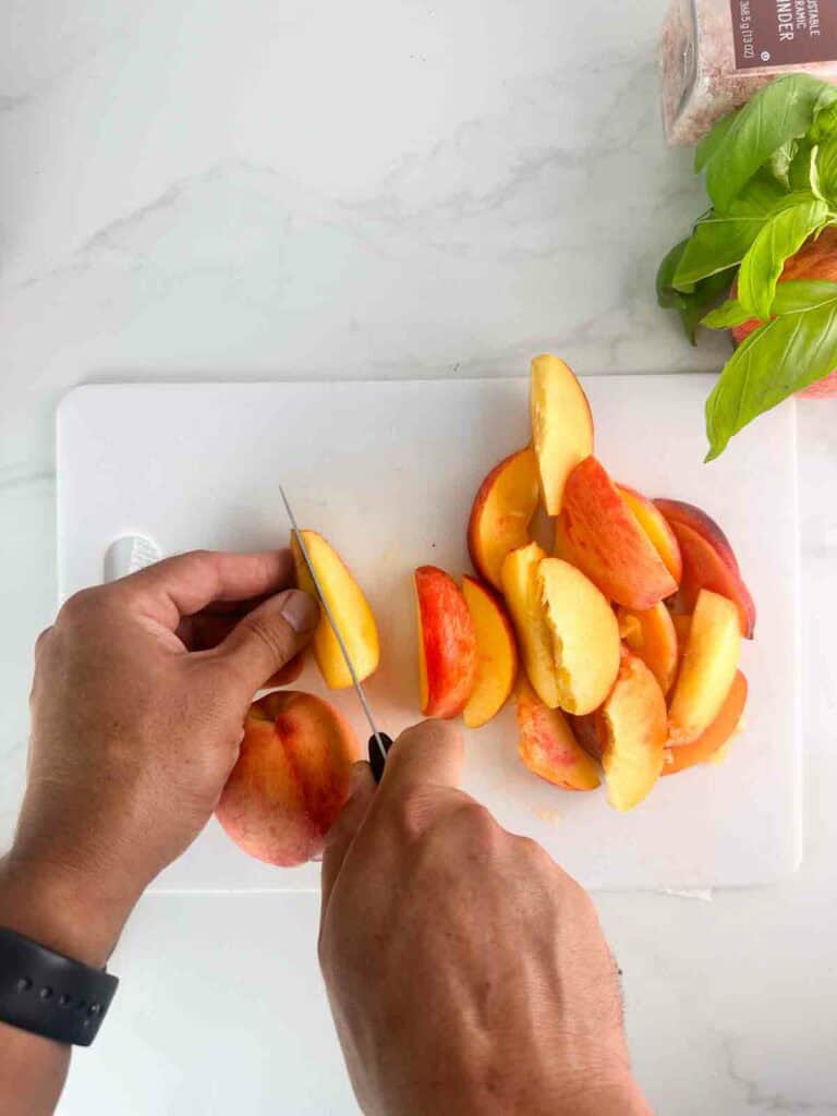Slicing peaches into slices on a white cutting board.