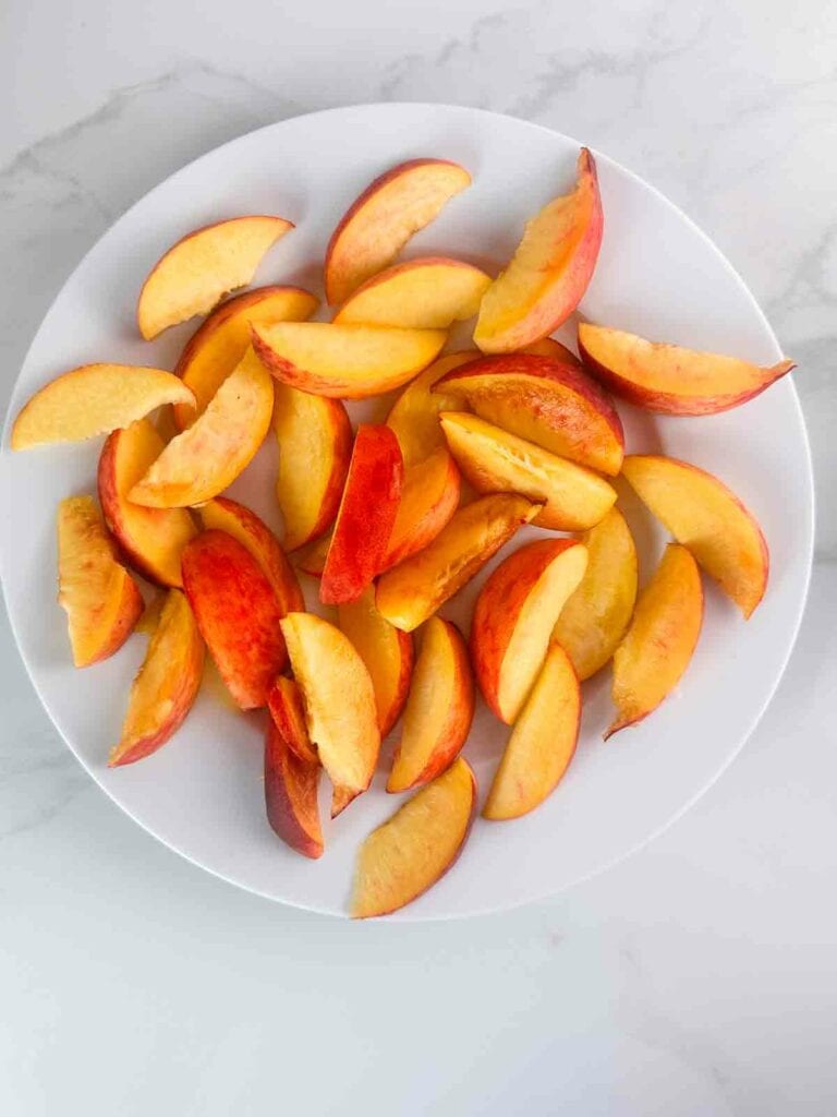 Peaches sliced into wedges on a white plate.