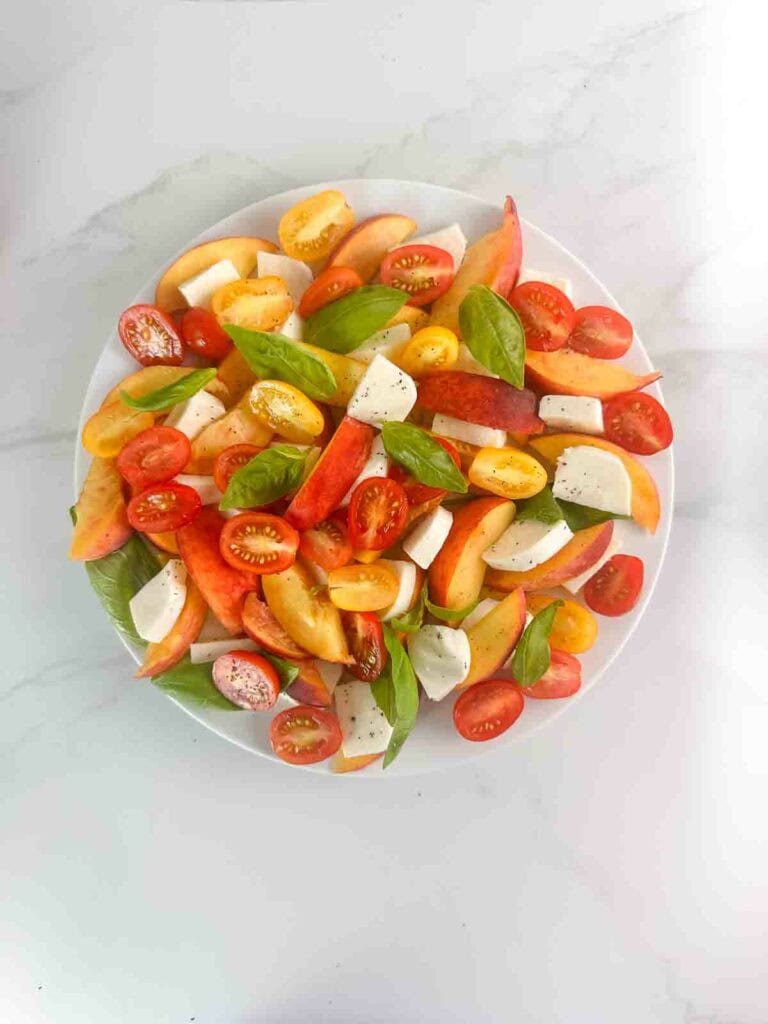 Peach caprese salad with peaches, sliced tomatoes, basil leaves, and cubed mozzarella cheese.