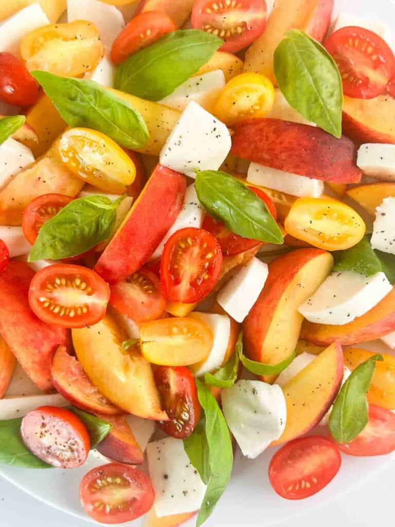 Peach caprese salad with peaches, sliced tomatoes, basil leaves, and cubed mozzarella cheese.