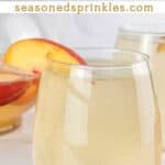 Peach sangria in wine glasses. Text reads: peach sangria, seasonedsprinkles.com
