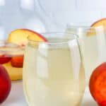 Peach sangria in wine glasses with peaches.