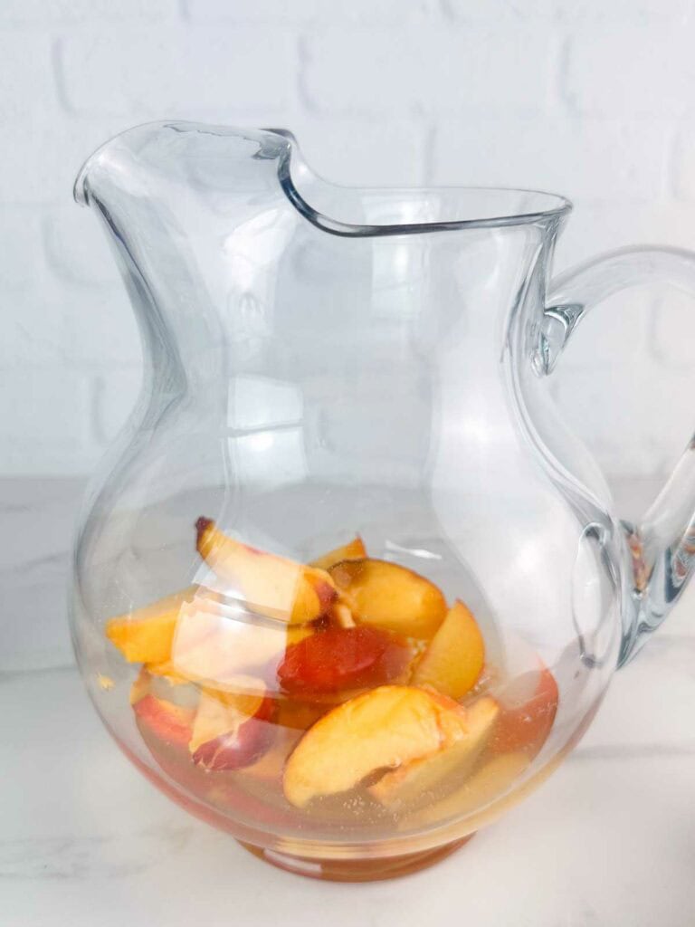 Peach slices in a pitcher to make peach sangria.