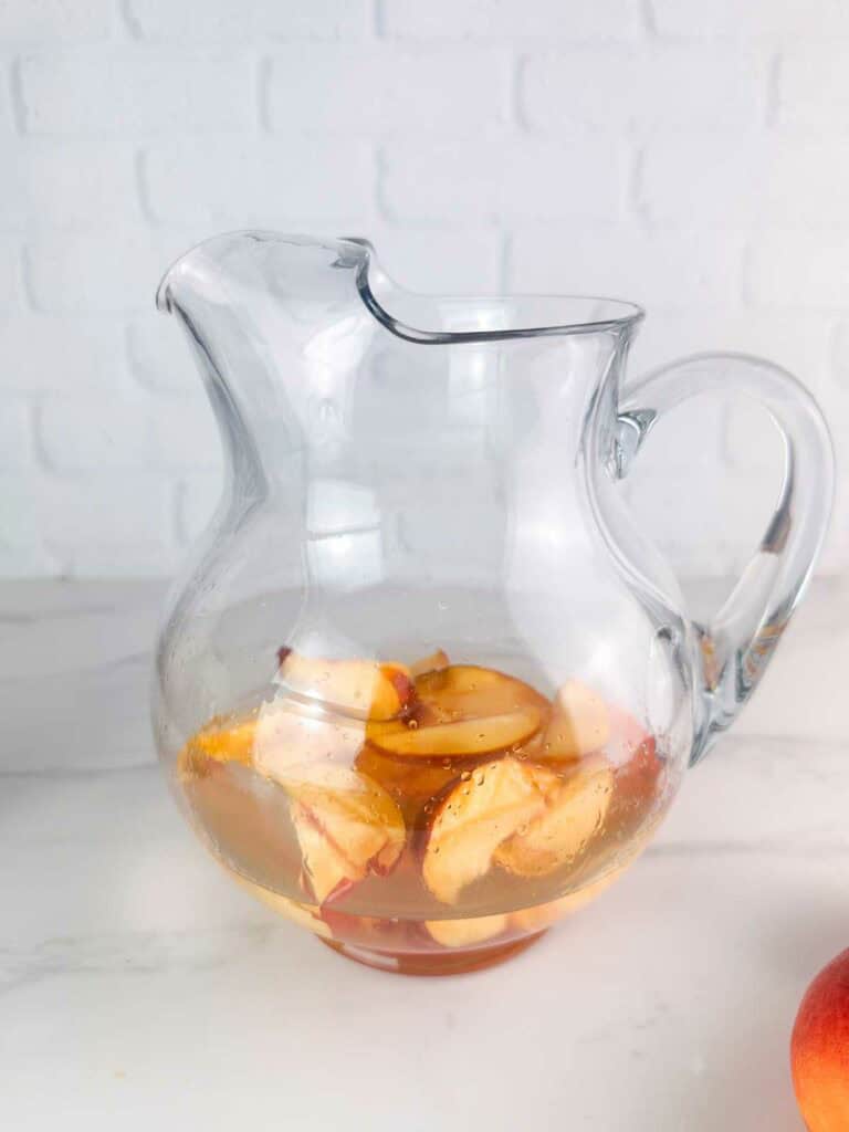 Peaches and simple syrup in a clear pitcher.