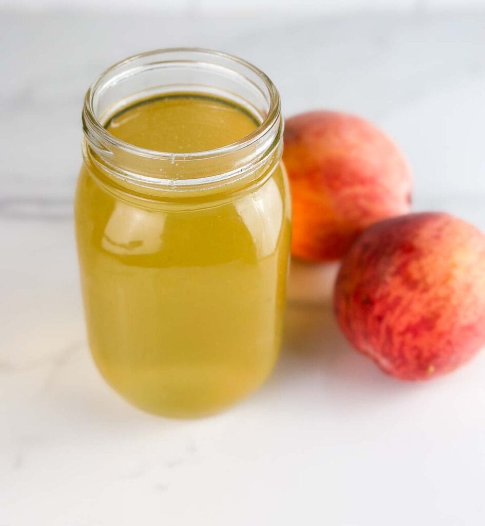 Peach simple syrup in a mason jar with peaches.