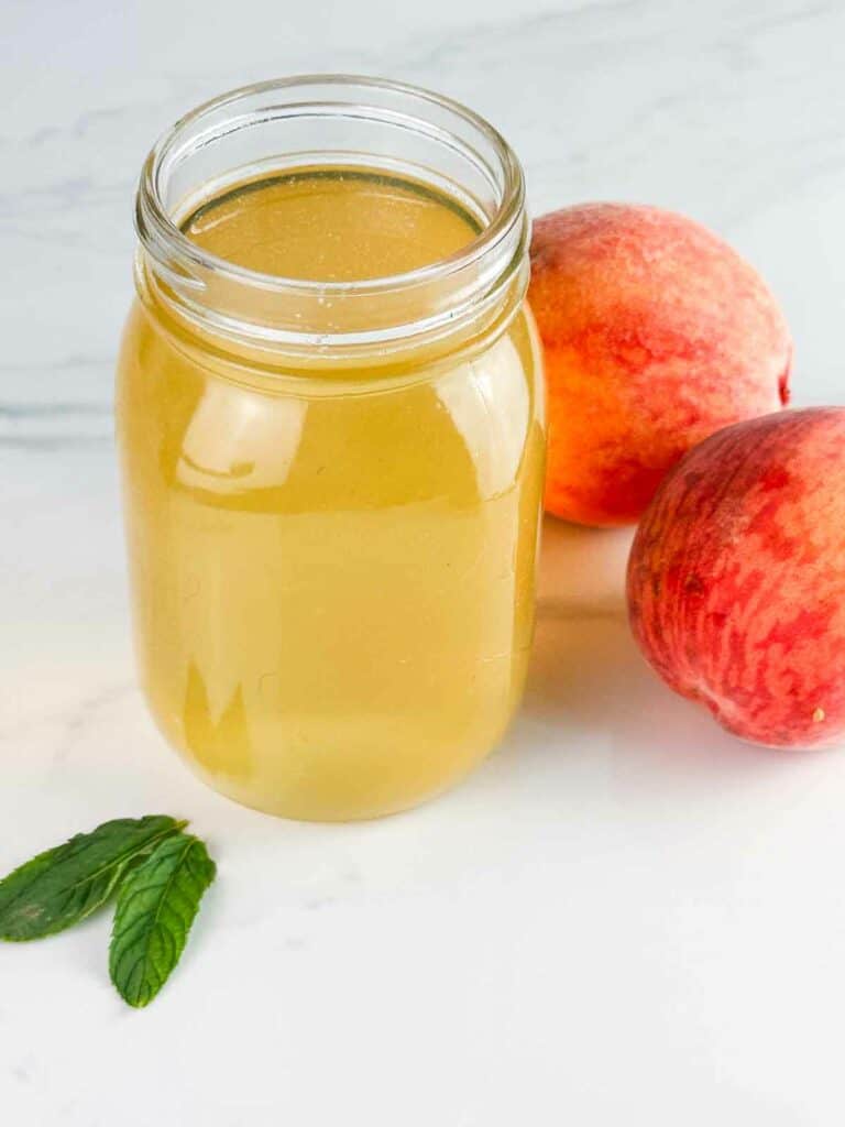 Peach simple syrup in a mason jar with peaches.