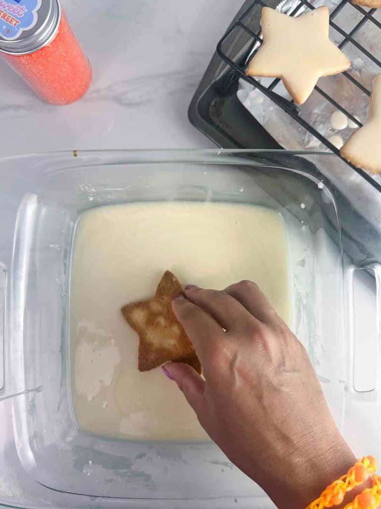 Dipping star shaped cookies into icing.