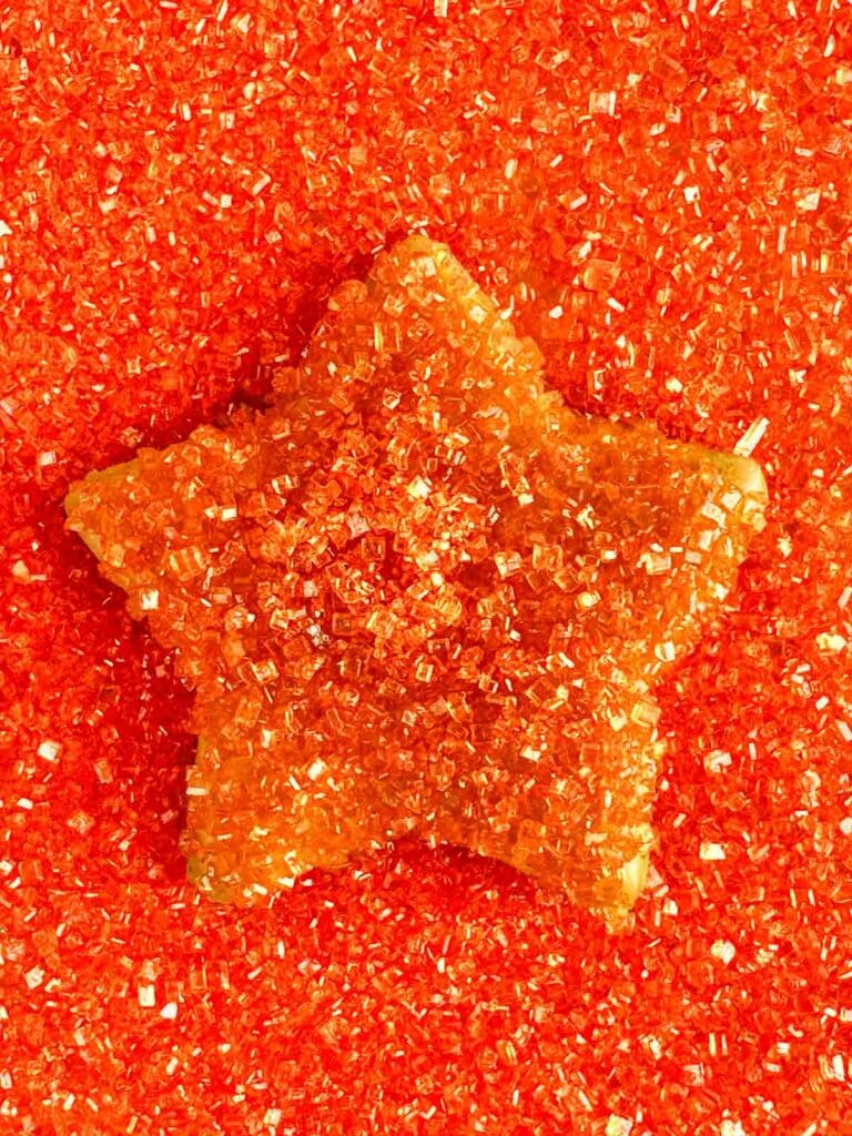 Star sugar cookie covered in and laying in orange glitter sprinkles.