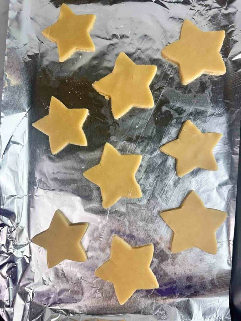 Star shaped sugar cookies on a aluminum foil lined cookie sheet.