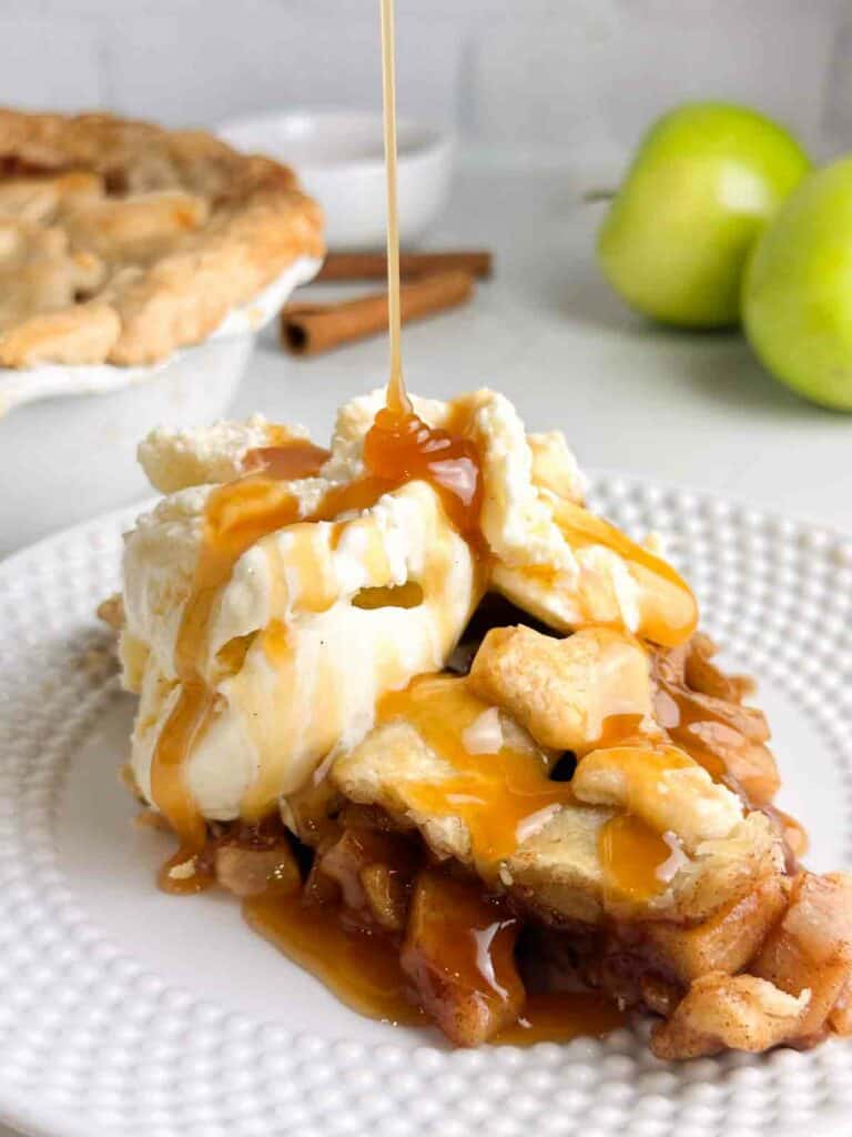 A piece from a homemade apple pie recipe topped with ice cream and caramel