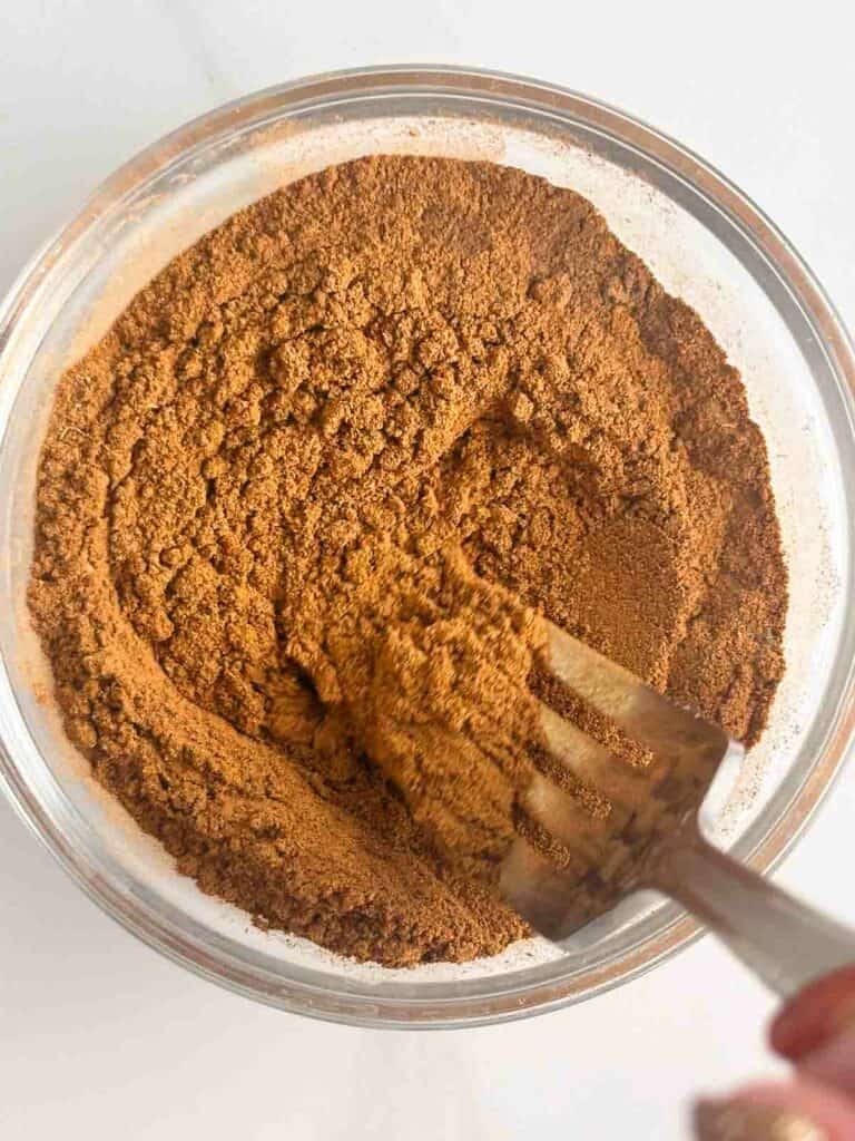 Mixing homemade apple pie spice with a fork in a small bowl.