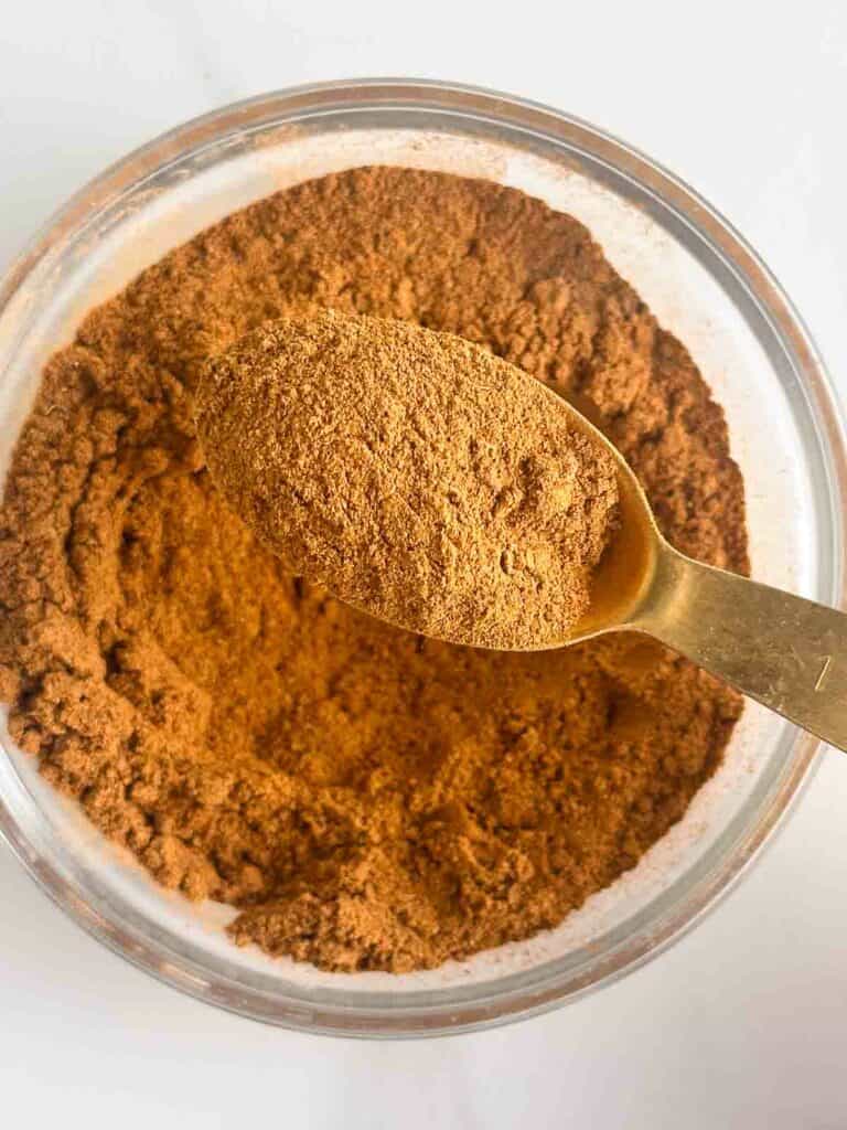Homemade apple pie spice shown in a spoon and bowl.