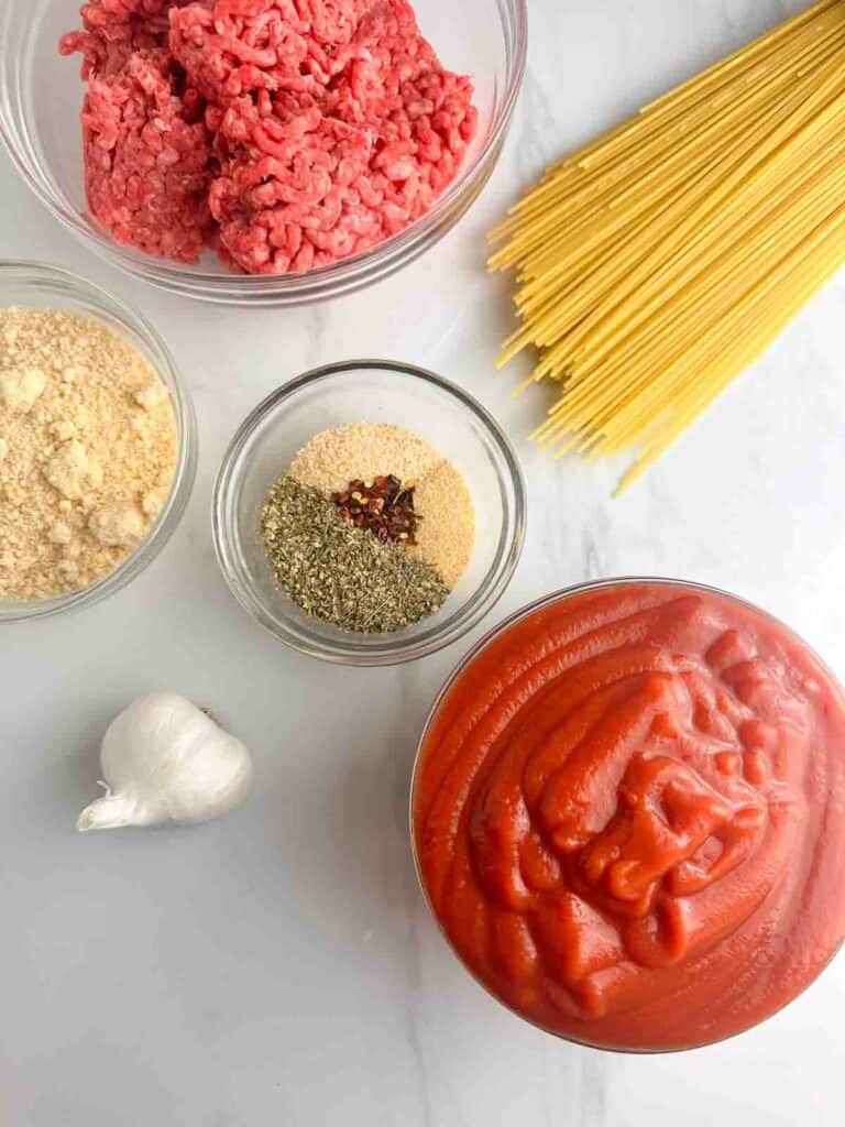 Ingredients for meat sauce: ground beef, grated parmesan cheese, garlic powder, onion powder, red pepper flakes, Italian seasoning, tomato puree, garlic, and spaghetti.