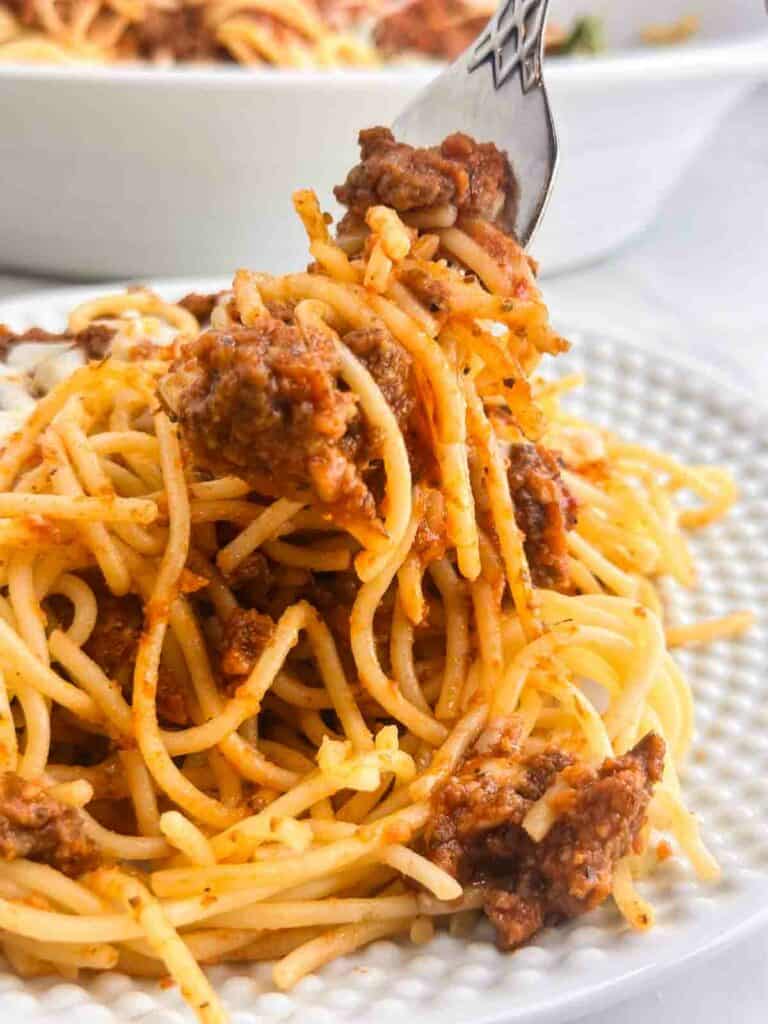Plated homemade meat sauce over spaghetti with a fork taking a portion.