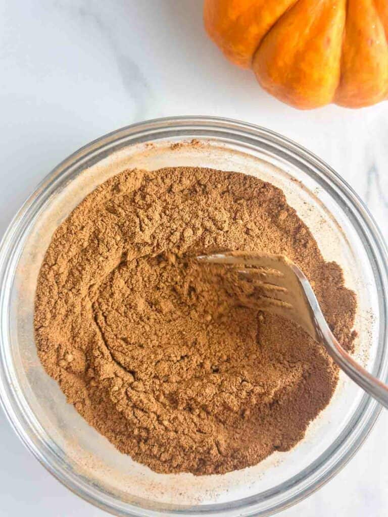 Using a fork to mix pumpkin pie spice in a small bowl.