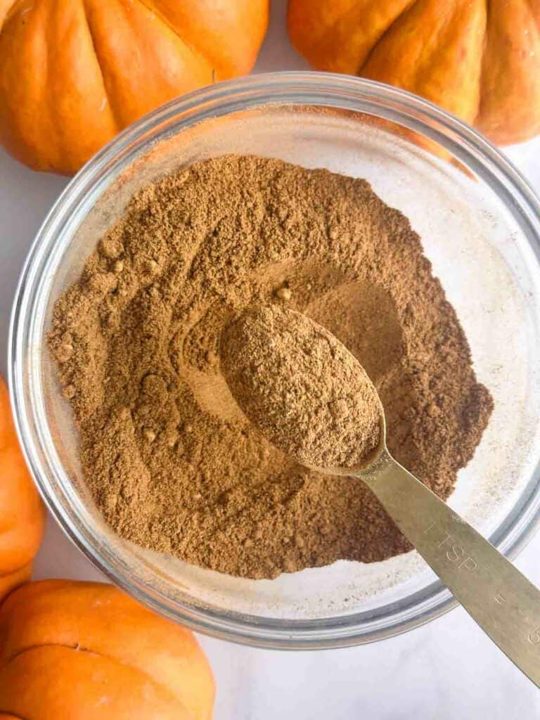 Spoonful of pumpkin pie spice over a small bowl.