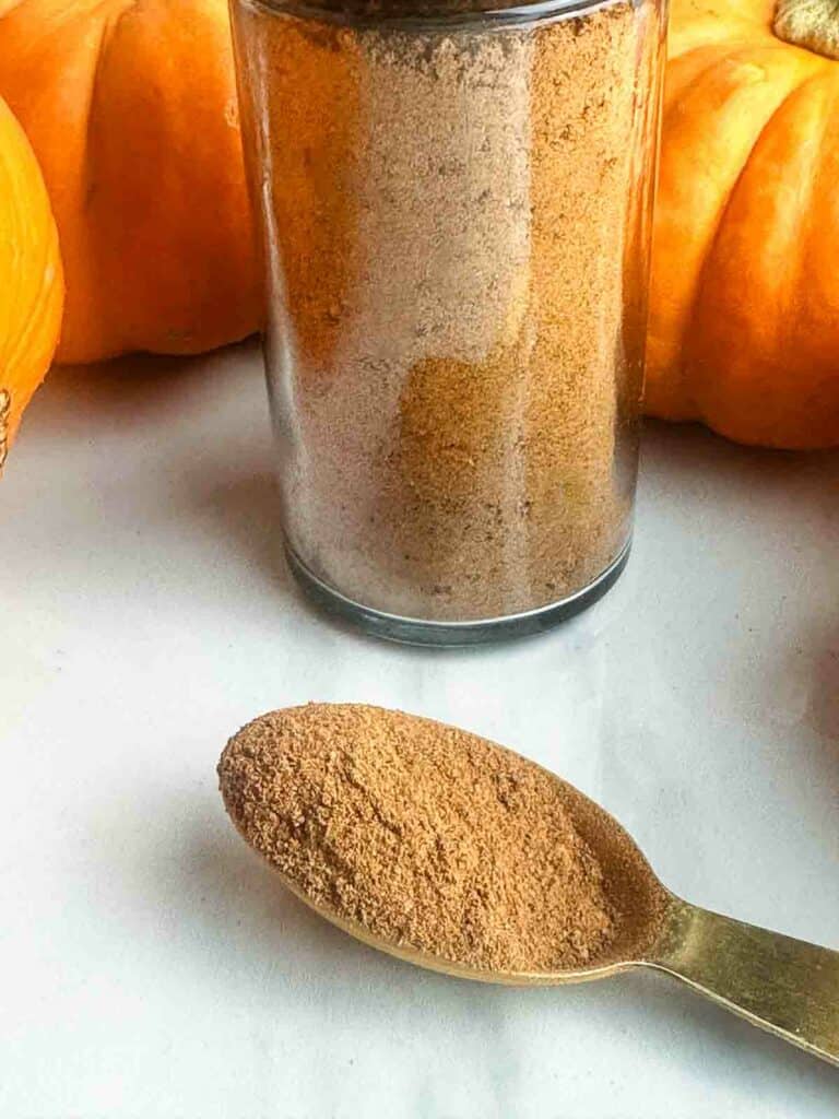 Homemade pumpkin pie spice recipe stored in a small jar with a spoon.