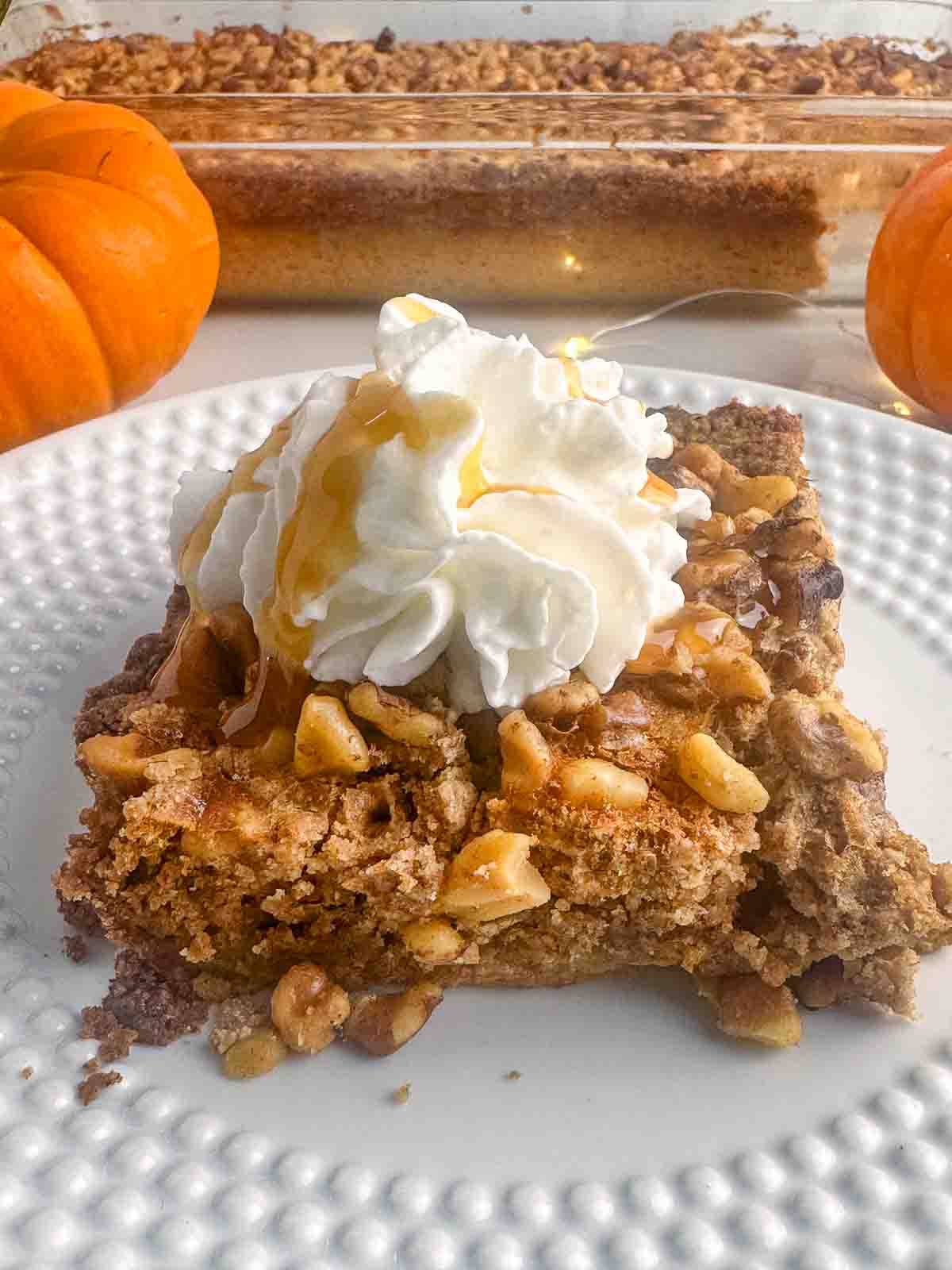 A casserole dish full of pumpkin praline cake with a whipped cream topped slice on a plate