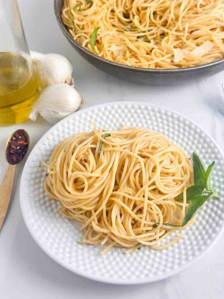 Serving of Spaghetti Aglio e Olio with the skillet and ingredients in the background.