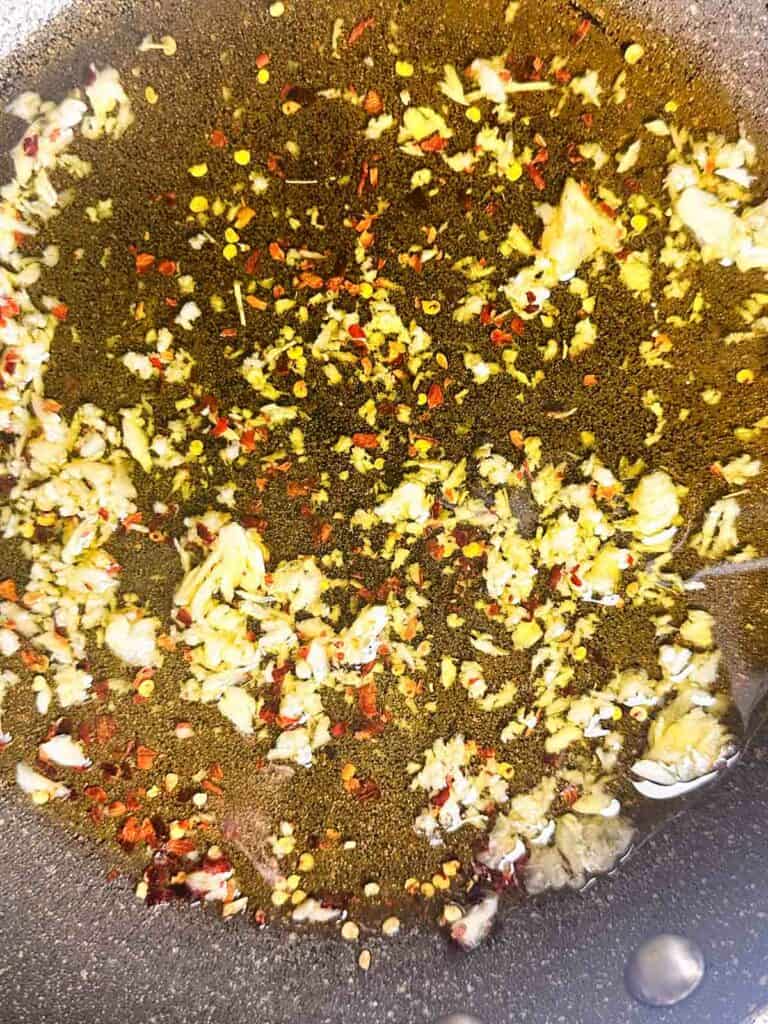 Adding red pepper flakes to garlic and olive oil.