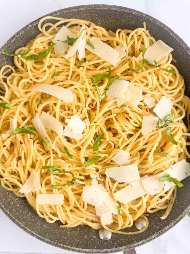 Spaghetti Aglio e Olio topped with fresh basil and parmesan cheese flakes in a skillet.