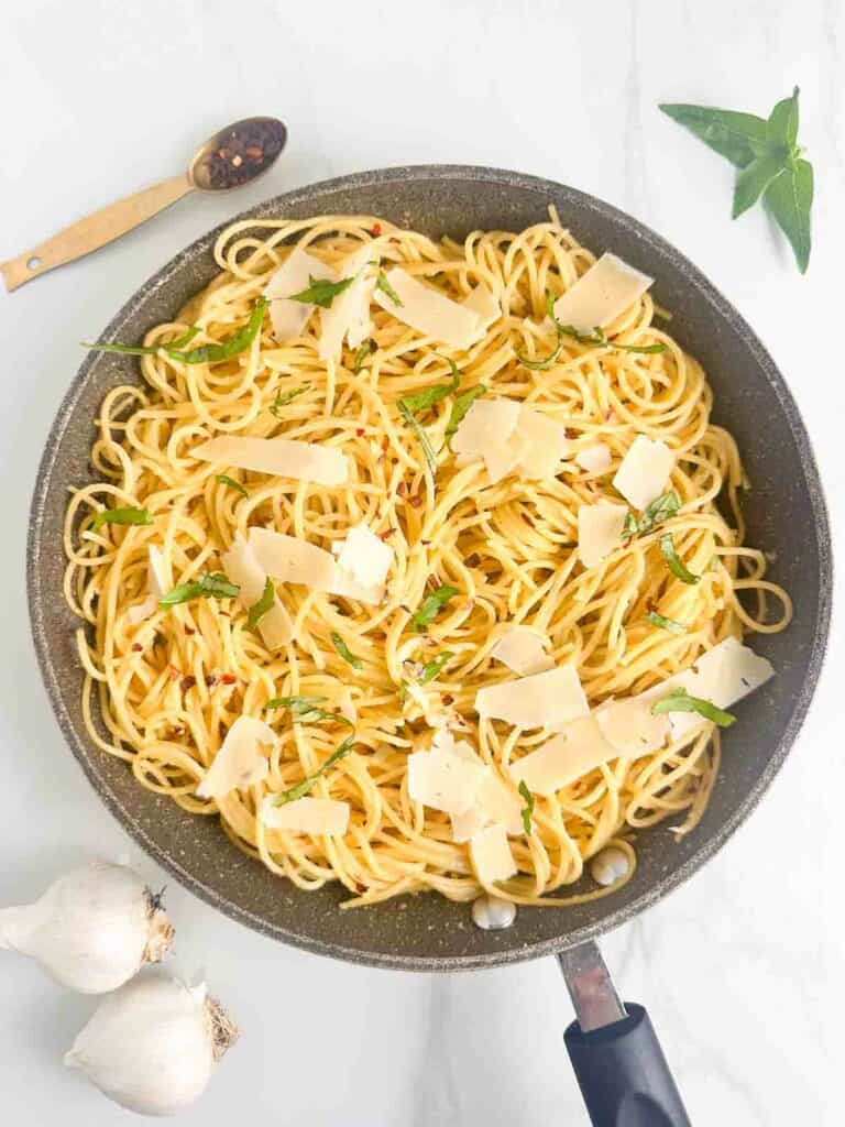 Spaghetti Aglio e Olio in a skillet with parmesan cheese and basil topping.