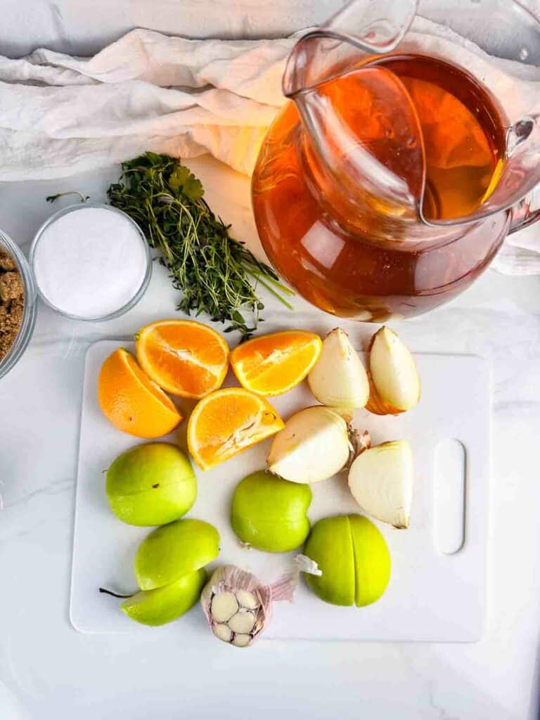Ingredients for apple cider turkey brine: apple cider, herbs, salt, brown sugar, oranges, onions, green apples, and garlic.