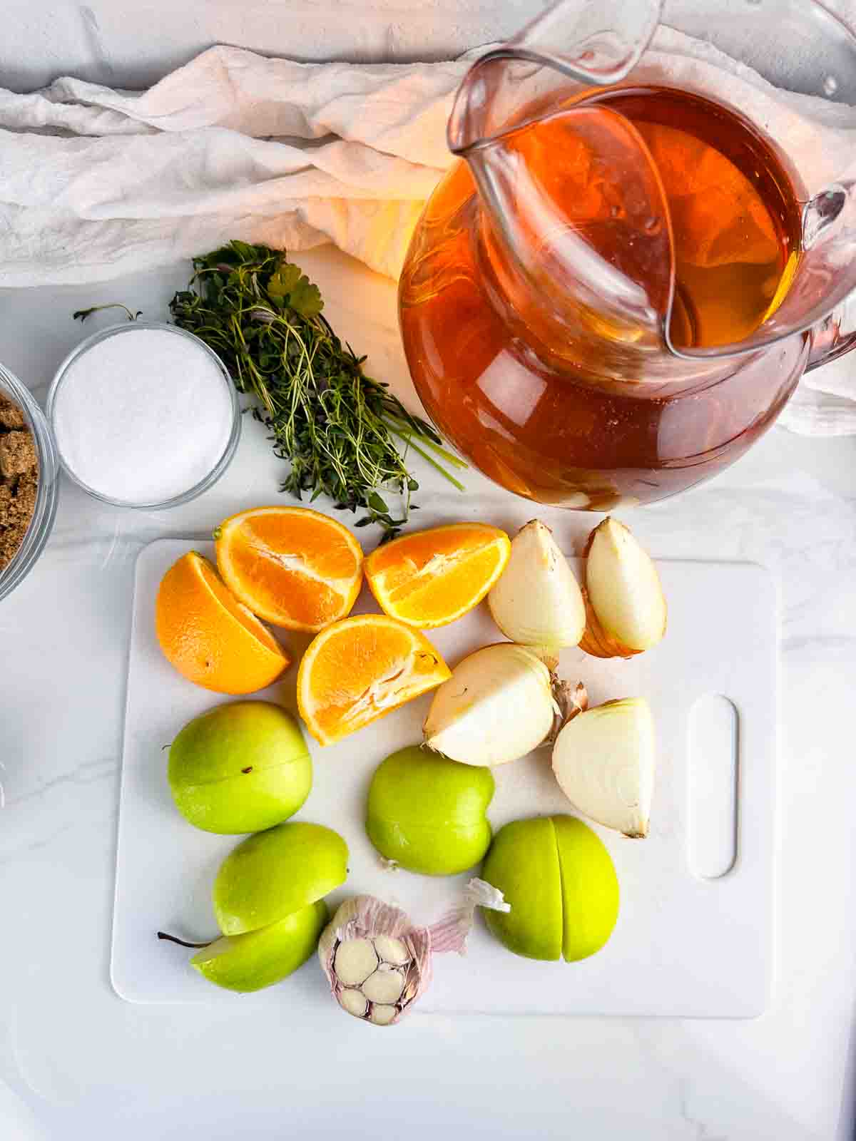 Ingredients for apple cider turkey brine: apple cider, herbs, salt, brown sugar, oranges, onions, green apples, and garlic.