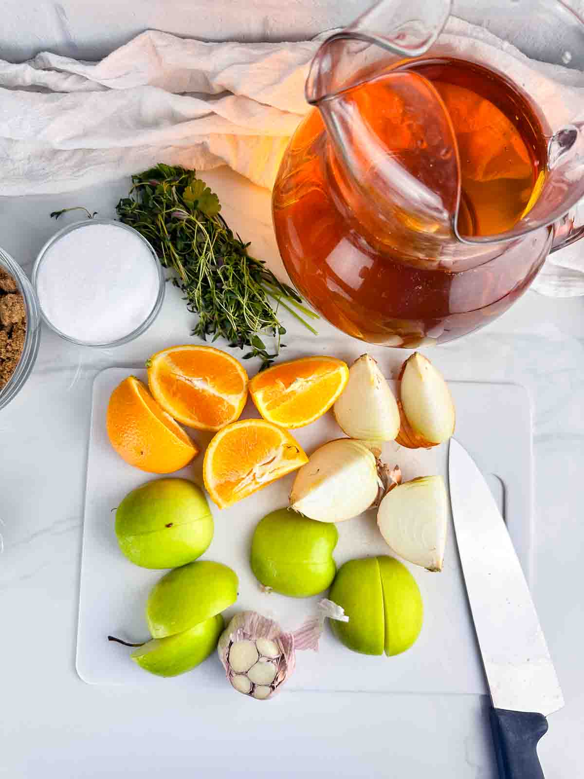 Ingredients for apple cider turkey brine: apple cider, herbs, salt, brown sugar, oranges, onions, green apples, and garlic.