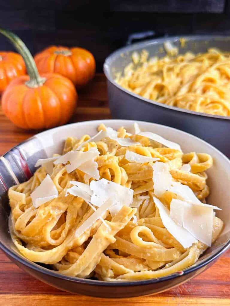 Bowl of pumpkin pasta with parmesan cheese on top with pumpkins in the background.