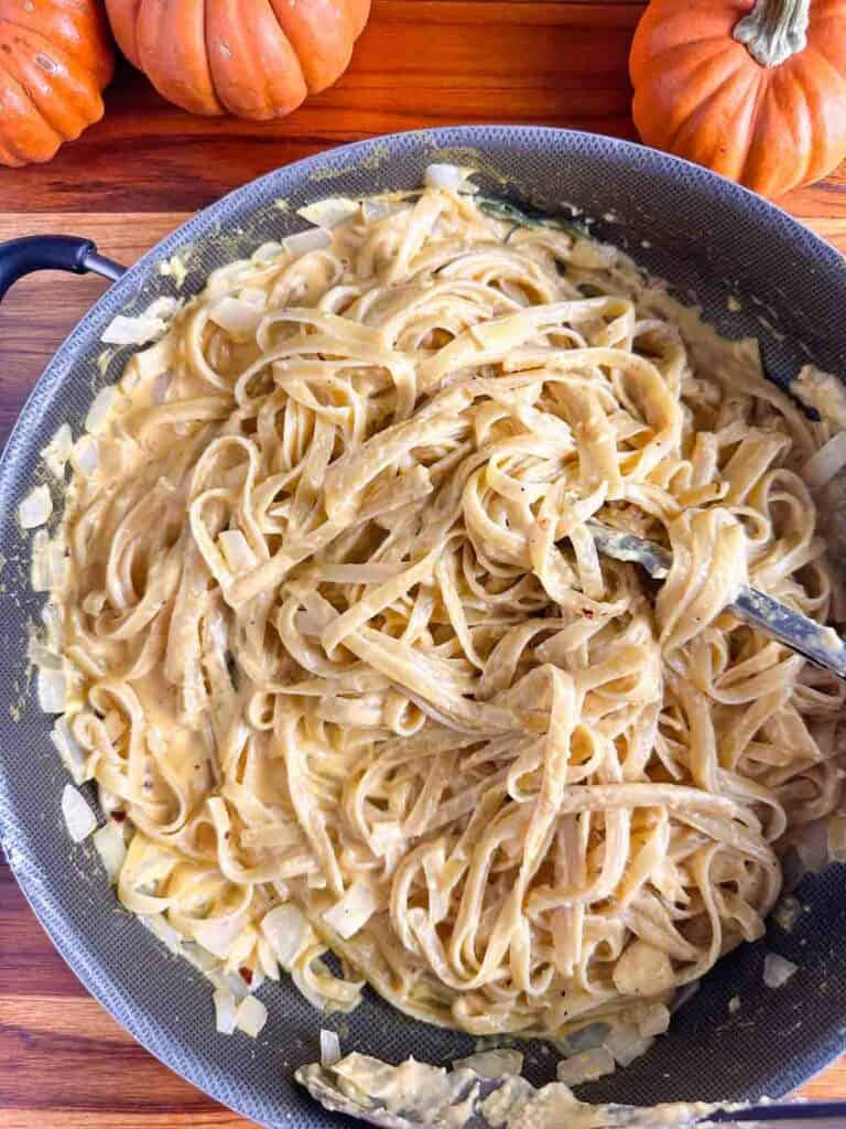 Pumpkin pasta in a pan with tongs.