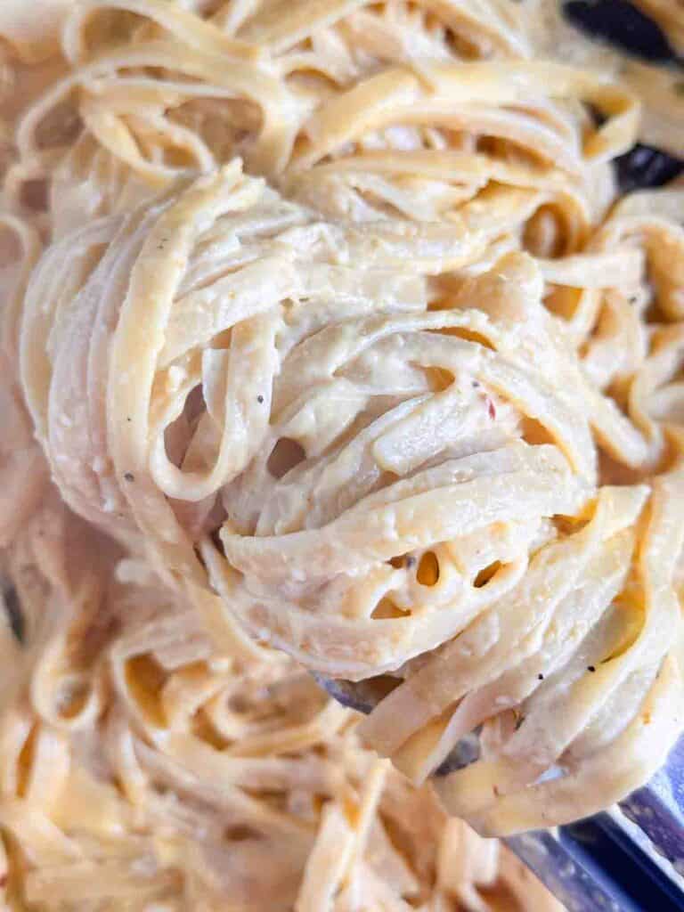 Pumpkin pasta held with tongs.