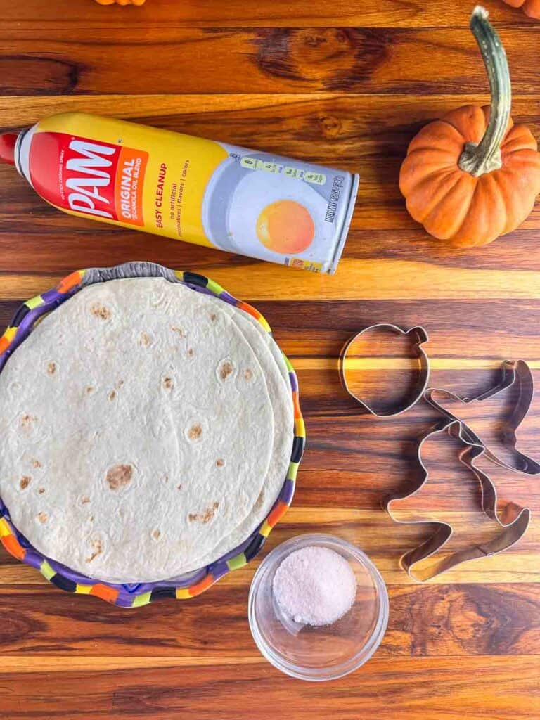 Ingredients and supplies for Halloween tortilla chips: flour tortillas, cooking spray, cookie cutters, and salt