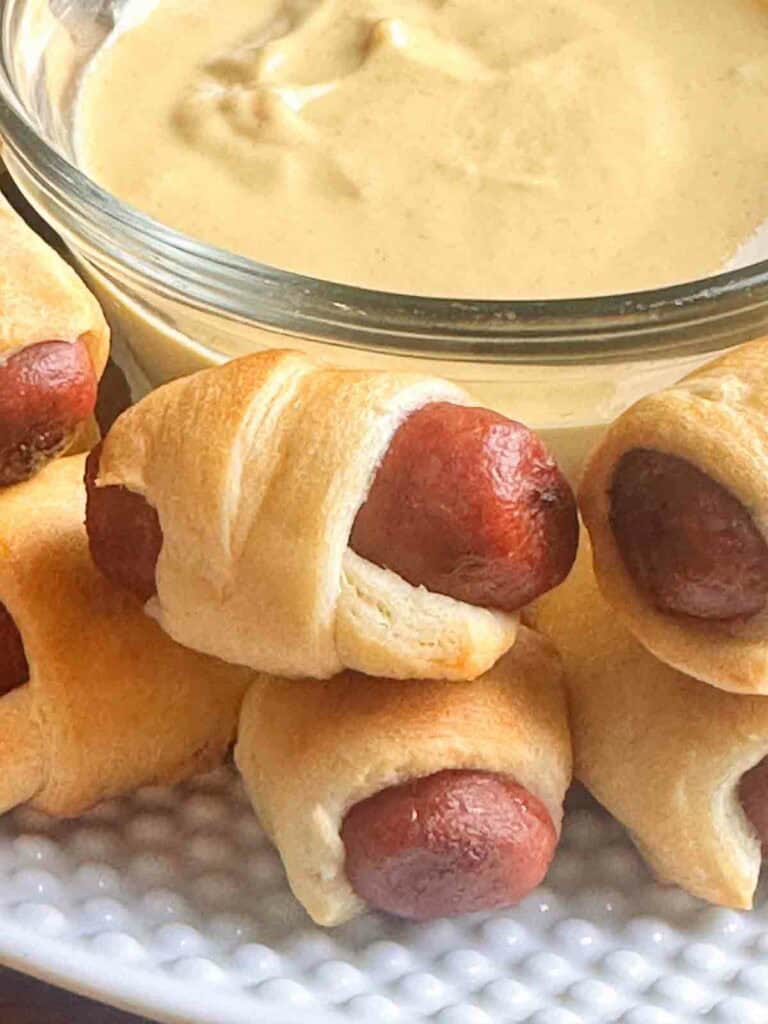 Pigs in a blanket next to mustard.