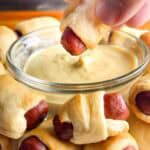 Pigs in a blanket being dipped into mustard.