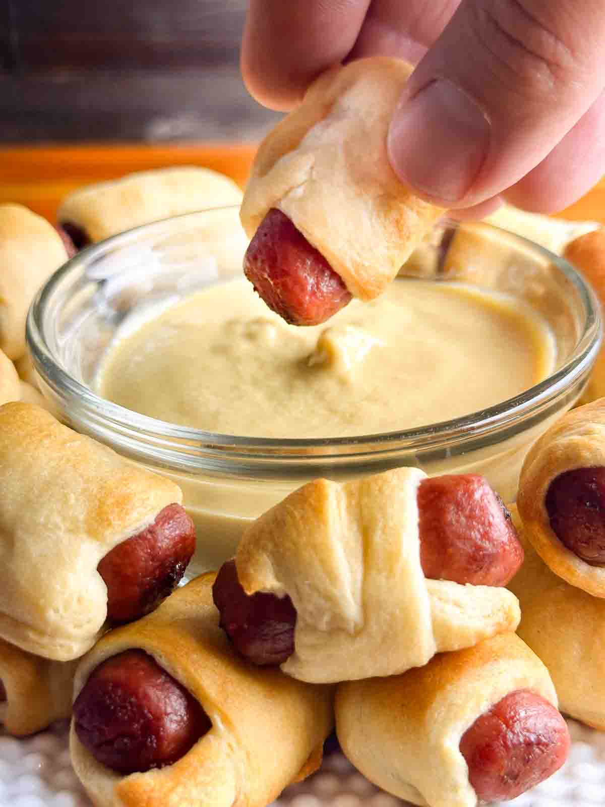 Pigs in a blanket being dipped into mustard.
